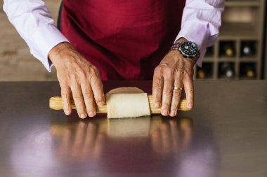 Şef hamuru paslanmaz çelik masada düzleştirmek için ahşap oklamalı iğne kullanıyor, aşçılık sınıfında pişirme tekniklerini gösteriyor.