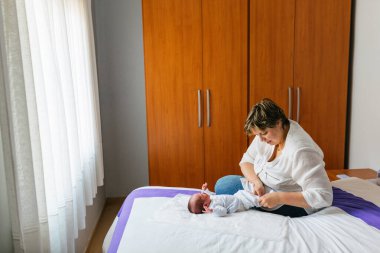 Anne bir aylık bebeğinin bezini değiştirirken yatak odasında bir yatakta oturuyor.