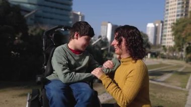 Serebral felçli bir anne ve çocuğunun güneşli bir parkta kucaklaşmaları ve sevgilerini paylaşmaları...