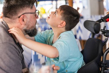 Serebral felçli bir çocuk lokantada yemek yerken babasına sevgiyle sarılıyor aile bağlarını ve engelliliğini gösteriyor.