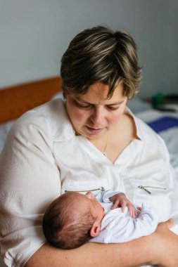 Anne bir aylık bebeğini nazikçe kucaklıyor, evlerinin rahatlığında sessiz bir bağ kurma anının tadını çıkarıyor.