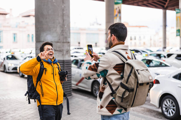 Two male tourists are taking photos and videos at a taxi station, potentially streaming live and sharing their travel experiences