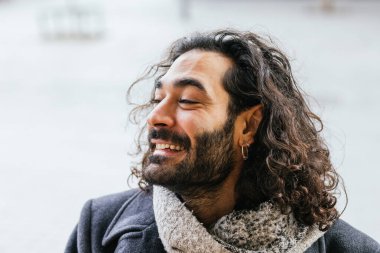 Uzun kıvırcık saçlı, sakallı, küpeli, gülümseyen ve kış gününün tadını çıkaran şık bir adamın portresi.