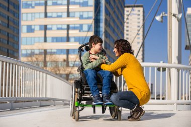 Tekerlekli sandalyede sakat kalmış mutlu bir çocuk şehrin sokaklarında keyifli bir yürüyüş yapıyor, sevgili annesiyle değerli anlarını paylaşıyor.