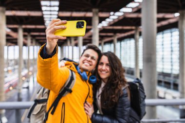 Tatile çıkmadan önce akıllı telefonuyla tren istasyonunda selfie çeken mutlu çift.