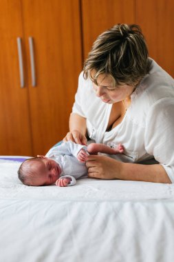 Anne, yeni doğan oğullarının altını değiştirirken evdeki yatakta yatarken günlük rutinlerinde şefkat ve şefkat anı yaratıyor.