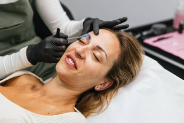 Güzellik uzmanı müşterilerin kaşlarını mikro patinaj işlemi için iplikle eşleştiriyor, profesyonel bir güzellik salonunda mükemmel bir simetri ve şekil sağlıyor.