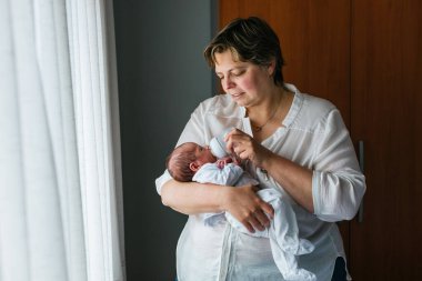 Sevgi dolu bir anne, bir aylık bebeğini kucaklarken, bir yandan da onu hafif bir odada besliyor.
