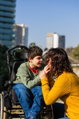 Sevgi dolu bir anne, oğluyla tekerlekli sandalyedeki engellilerle etkileşime girer, açık havada güneşli bir günün tadını çıkarır.