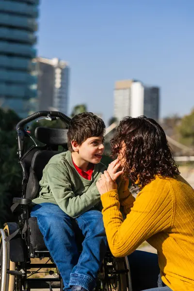 Sevgi dolu bir anne, oğluyla tekerlekli sandalyedeki engellilerle etkileşime girer, açık havada güneşli bir günün tadını çıkarır.