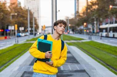 Modern şehirde tramvay durağında beklerken sırt çantasında klasörler olan kendinden emin üniversite öğrencisi.