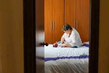 Anne bir aylık bebeğinin bezini yavaşça değiştiriyor, rahat bir yatak odasında yatakta uzanıyor, şefkatli anları kucaklıyor.