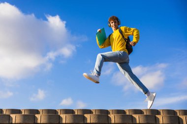 Dışarıda koşuşturan enerjik üniversite öğrencisi müzik dinlerken, kitap ve sırt çantası tutarken, özgürlüğü, eğitimi ve gençlik dinamizmini simgeliyor.