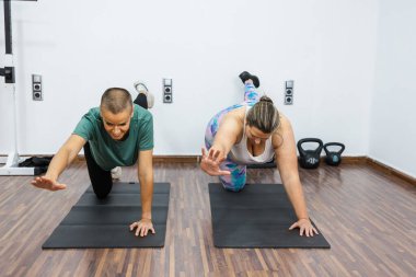 Kilolu bir kadın kişisel antrenörüyle vücut egzersizleri yapıyor. Spor salonunda güç ve istikrar kazanmaya odaklanıyor.