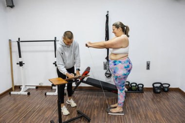 Beslenme uzmanı bir kadın müşteriyi spor salonunda tartıyor ve notlar alıyor, ona kişisel fitness planında yardım ediyor.