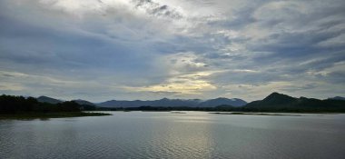 Gümüş gökyüzünde gün batımı akşam gölde ve dağ manzarasında.