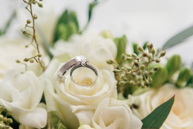 Wedding rings lie on a beautiful bouquet as bridal accessories. Close-up view of golden wedding rings and beautiful small blue flowers on wooden tabletop