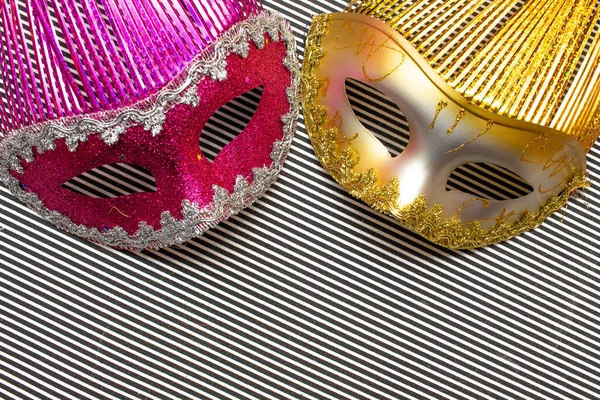 golden  ad pink carnival masks on a black and white striped background  and colorful flowers
