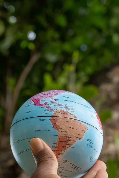 hand holding a terrestrial globe with green texture background  showing South and North america