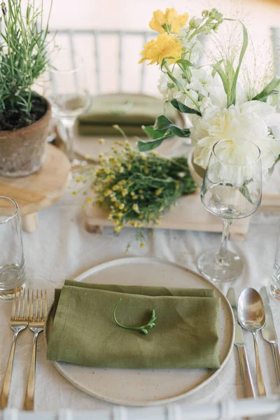 Festive table setting for a garden event. Serving plate with green rustic table cloth and spring blossom decoration. Earthy colors style arrangements.