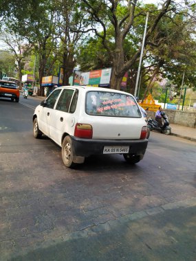 Bangalore, Karnataka, Hindistan-Mar 20 2020: Kannada Film Aktörü Asi Yıldız Ambarish Etiketi ve Beyaz Maruti Zen Arabası 'ndan alıntılar. Büyük Ağaçlar, Gölgeler ve Şehir Manzaralı Bangalore Asfalt Yolu.