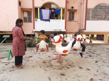 Bangalore, Karnataka, Hindistan-3 Mart 2024: Dairelerin yakınındaki oyun parkında annelerinin yardımıyla oynayan üç kişilik bir grup.