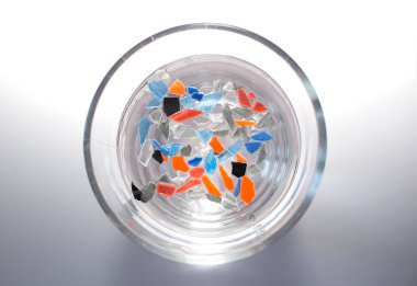 İçinde küçük ve renkli plastik parçalarının yüzdüğü bir bardak su. Plastik ürünler ve parçaları tüm gezegeni kasıp kavuruyor.. 