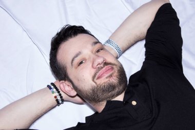 Rahat bir adam elleri başının altında sırt üstü yatar. Yakışıklı adam objektifin önünde poz veriyor ve dinleniyor..