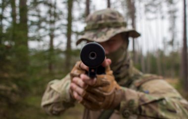 Genç bir adam (belki de bir asker) kısa namlulu bir ateşli silah ateşler..