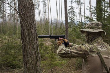 Genç bir adam (belki de bir asker) kısa namlulu bir ateşli silah ateşler..
