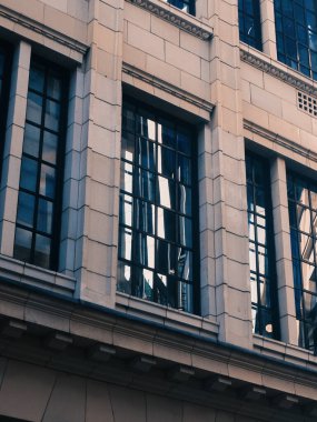 Londra, İngiltere - 28 Eylül 2024: Neoklasik ofis perdesindeki yansıtıcı cam pencereler Londra şehrinin göbeğindeki yakın gökdelenleri yakalıyor