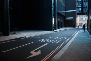 Londra, İngiltere - 28 Eylül 2024: Yalnız bir insan, Londra şehrinin karanlık mimarisi ile çevrili, sessiz ve gölgeli bir modern caddede yürüyor.