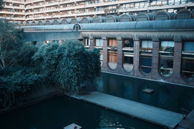 Londra, İngiltere - 28 Eylül 2024: Lakeside geçidi ve Londra 'daki Barbican Malikanesi' nin eğri büğrü pencereli konutlarının yanında aşırı gelişmiş yeşillik.