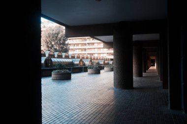 Londra, İngiltere - 28 Eylül 2024: Londra şehrinde beton sütunlar ve cam kubbelerin yer aldığı Barbican Malikanesi 'nde kapalı bir yürüyüş yolunda mimari simetri ve gölge desenleri.