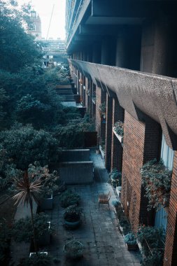 Londra, İngiltere - 28 Eylül 2024: Barbican Evleri 'nin ekiciler, yeşillikler ve St. Giles Cripplegate Kilisesi' nin uzaktaki Brutalist yerleşim alanları manzarası