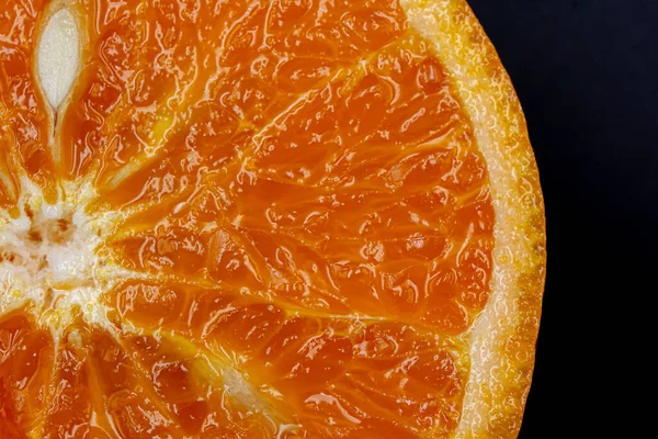 Oranges on a black background. One orange is cut in half close up, the other is whole.
