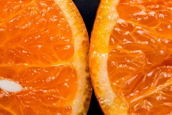 Oranges on a black background. One orange is cut in half close up, the other is whole.