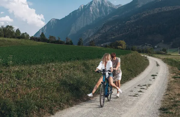 两个朋友或夫妇正在沿路骑车 运动和积极生活的日落时间概念 情侣们学习骑自行车 一起玩乐 在城市附近的山上旅行 免版税图库图片