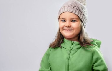 Portrait of the child in warm clothes and a hat on the gray background