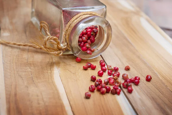 Pink pepper spilled out of a jar on a wooden surface