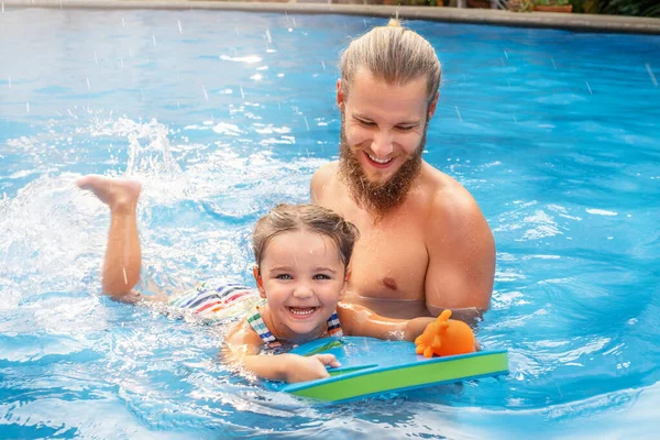 Çocuk babasıyla havuzda yüzmeyi öğreniyor.