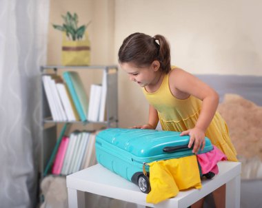 Bir çocuk mavi bir bavulu tatil eşyalarıyla kapatmaya çalışır.