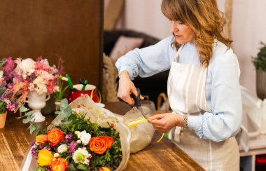 Çiçekçi, çiçekçi dükkanında canlı bir buketi dikkatlice sarıp sarmalar. Çiçek sektöründe küçük bir işletme sahibi..