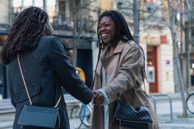 İki Afrikalı etnik arkadaş bir şehir merkezinde el sıkışıyor, gülümsüyor ve birbirlerini selamlıyorlar.