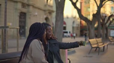 Şehir parkında selfie çeken iki neşeli genç kadın.