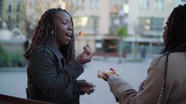 İki genç Afrikalı kadın Avrupa şehir meydanında birlikte meyve atıştırıyor.
