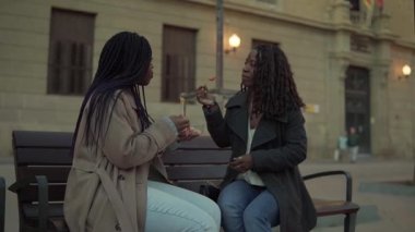 İki arkadaş birlikte bir bankta oturup atıştırmanın tadını çıkarıyorlar.