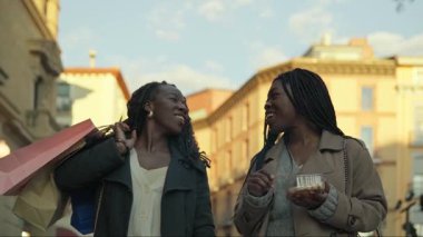 Two happy african friends enjoying a snack while walking through a city center after a shopping spree