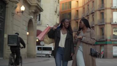 Neşeli arkadaşlar alışveriş torbaları taşırken atıştırmanın tadını çıkarıyorlar.