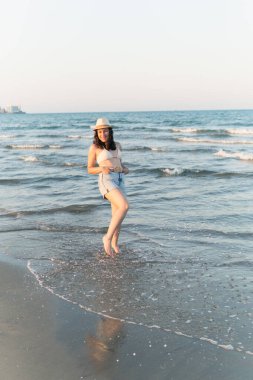 Yaz tatilinin tadını çıkaran bir turist gün batımında sahilde yürüyor.